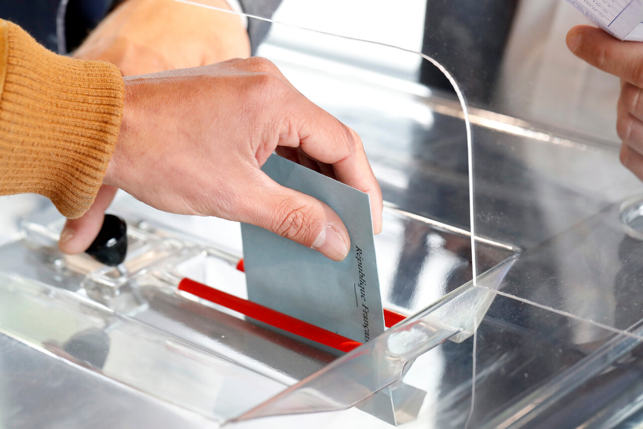 Image d'une personne déposant une enveloppe dans une urne pour voter